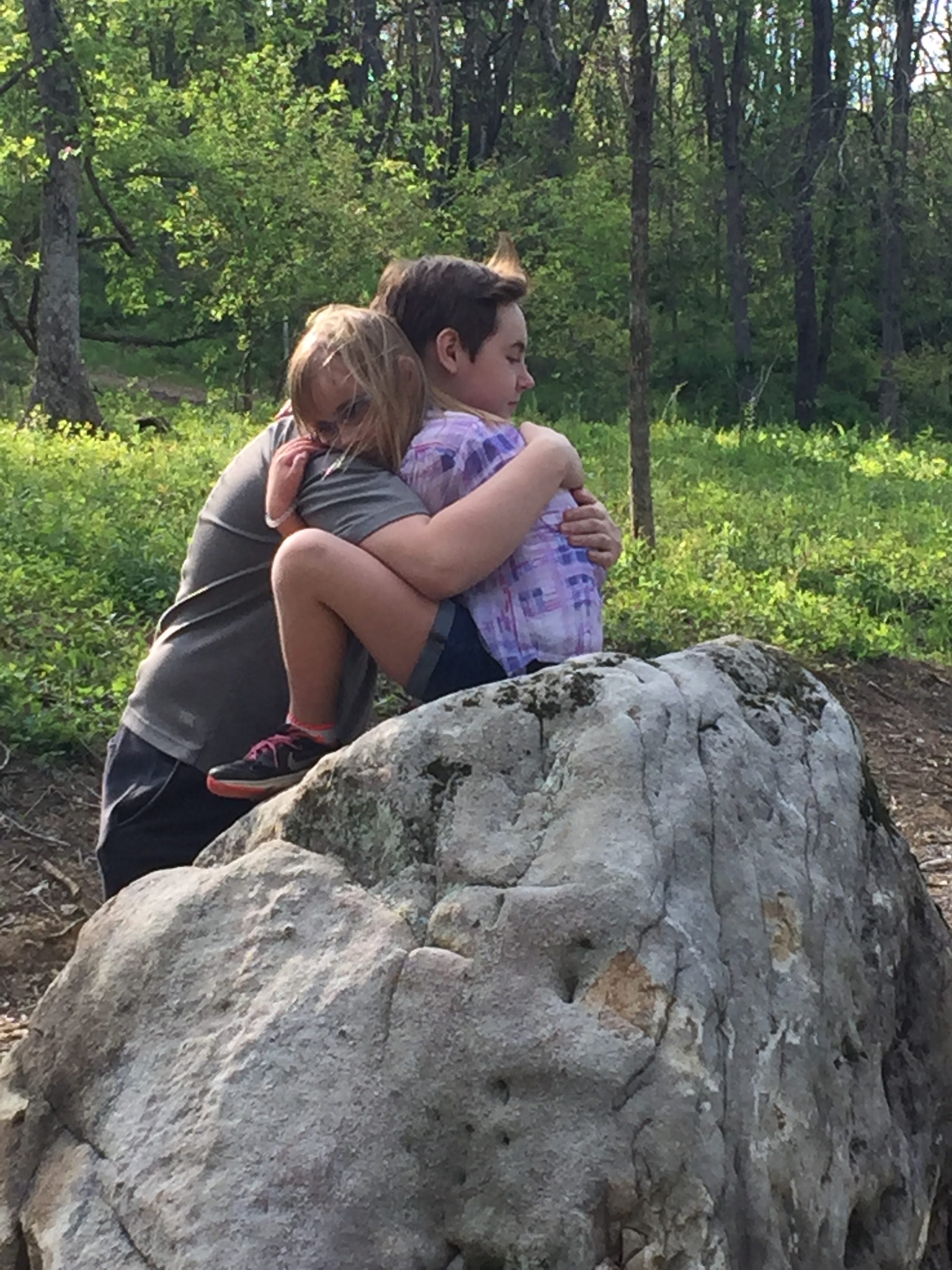 A person hugging a young person on a rock
