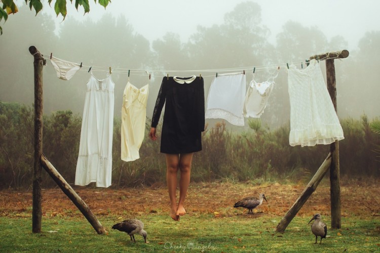 A photograph of an outdoor clothesline with white clothes hanging, and one black dress on which legs are hanging