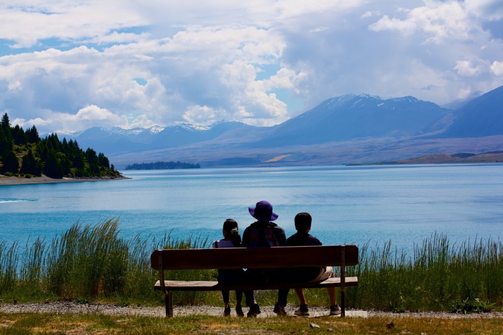 from behind, grandmother sits with two children overlooking a lake