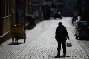 A person with a grocery bag stands alone in a street.