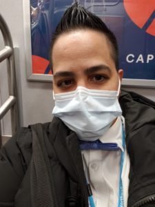 POC with short hair and wearing a surgical mask on the subway.