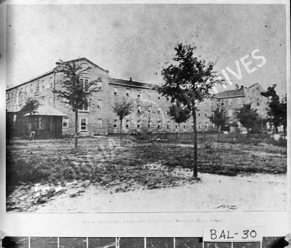 A black and white image of an asylum with a few trees in front.