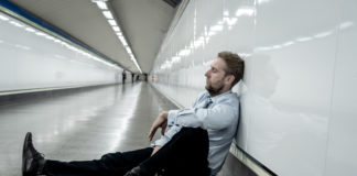 Social Determinants of Health and the Continued Individualization of Suffering man sits on floor against wall of tunnel