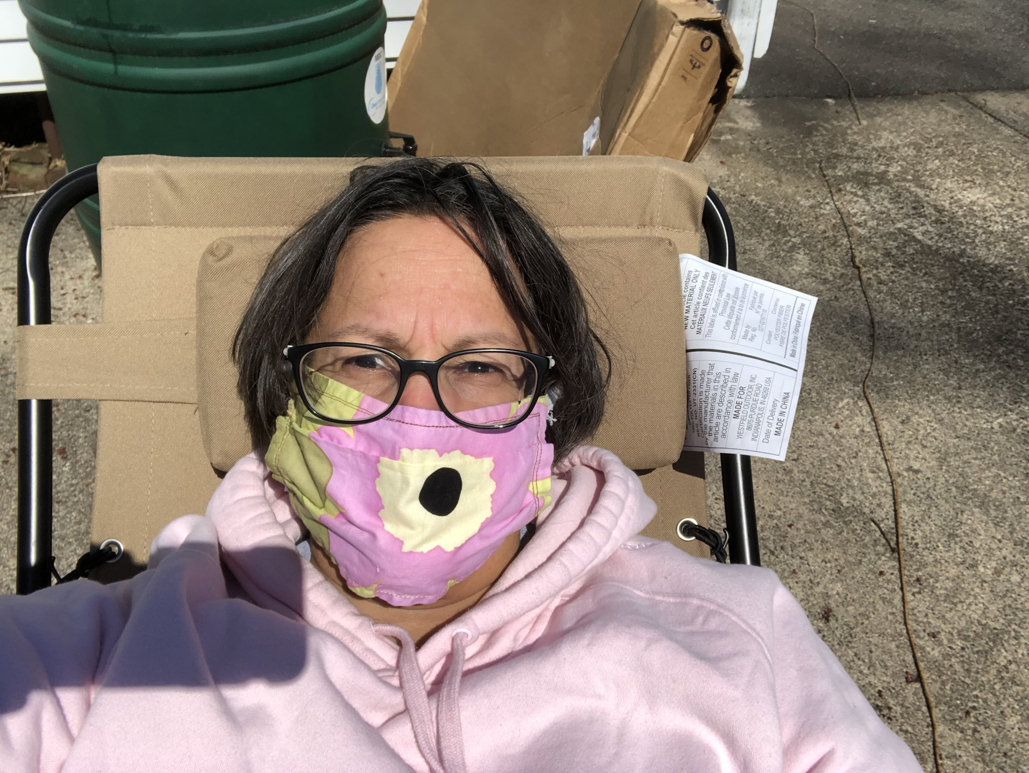 A woman with chin-length brown hair wears a pink jacket smiles through a pink mask.