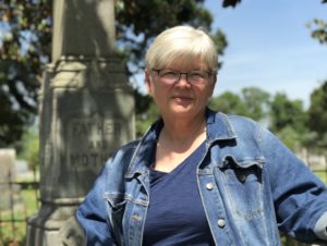 A white woman with short blonde hair and glasses wearing a denim jacket.