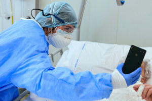 A masked doctor holds a phone up to a patient's face.