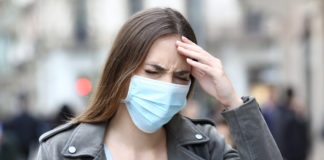 Is COVID-19 Making Everybody Crazy? woman holding her head annoyed wearing medical mask