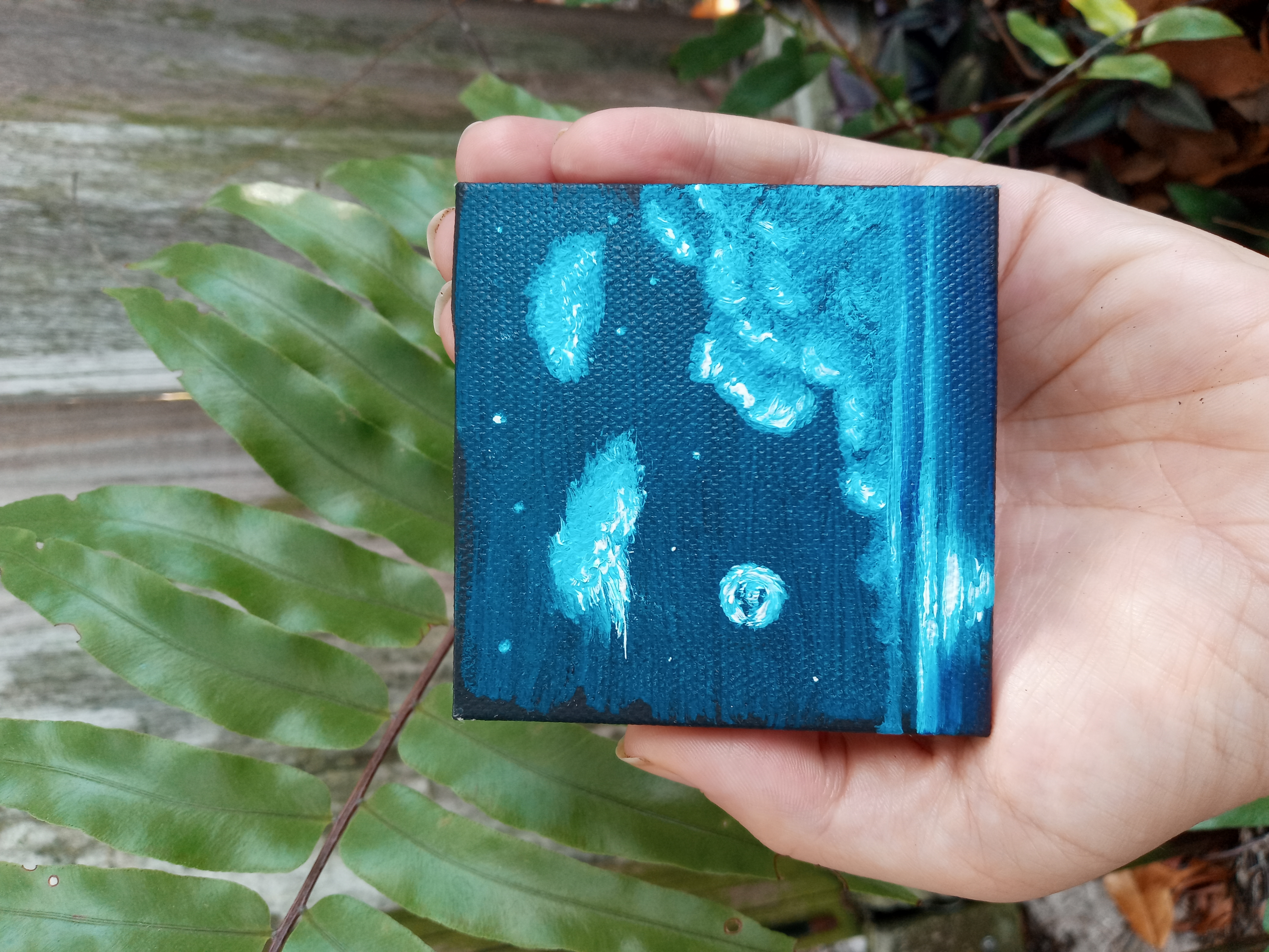 A hand holding a small painting of the night sky