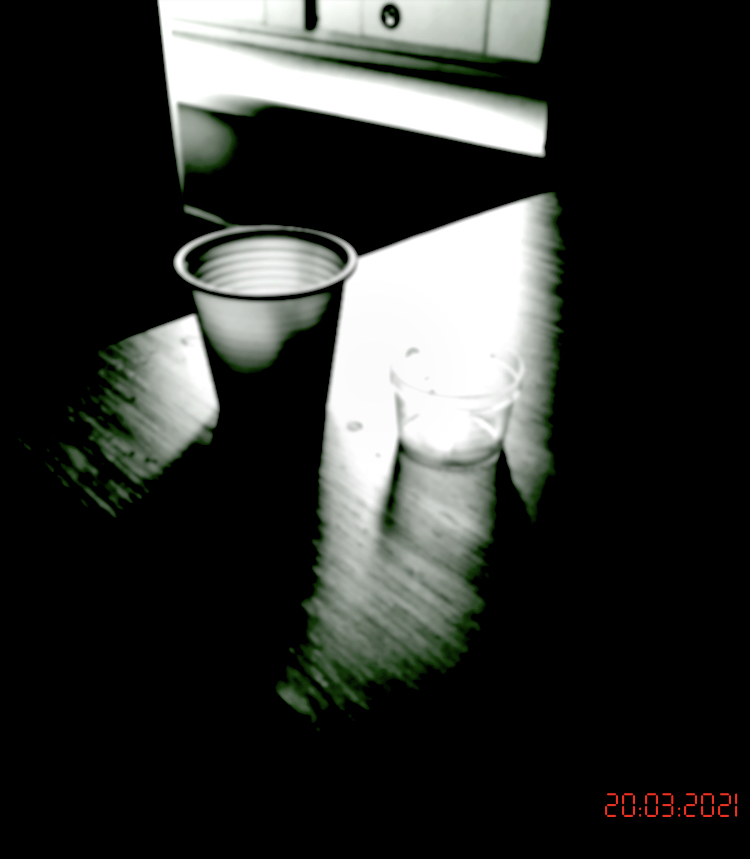 A dark, time stamped, photo of a plastic cup and pills on a table