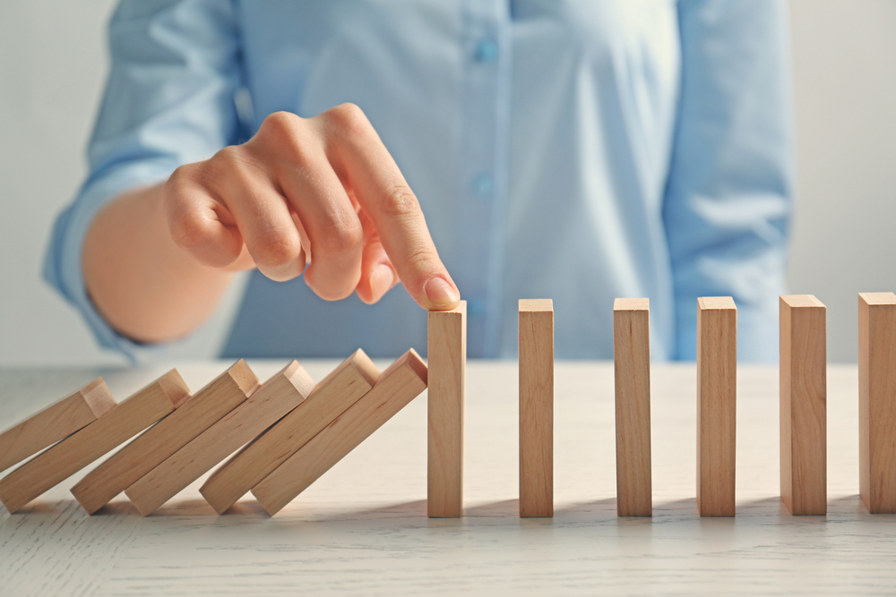 Businesswoman hand trying to stop toppling dominoes on table