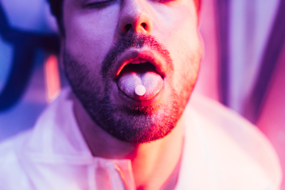 Photograph of man's lower face with a pill on his tongue