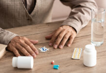 Researchers Debate the FDA’s Controversial Alzheimer’s Drug Approval A paper with a question mark on it rests between some pills and a man's hands on a table