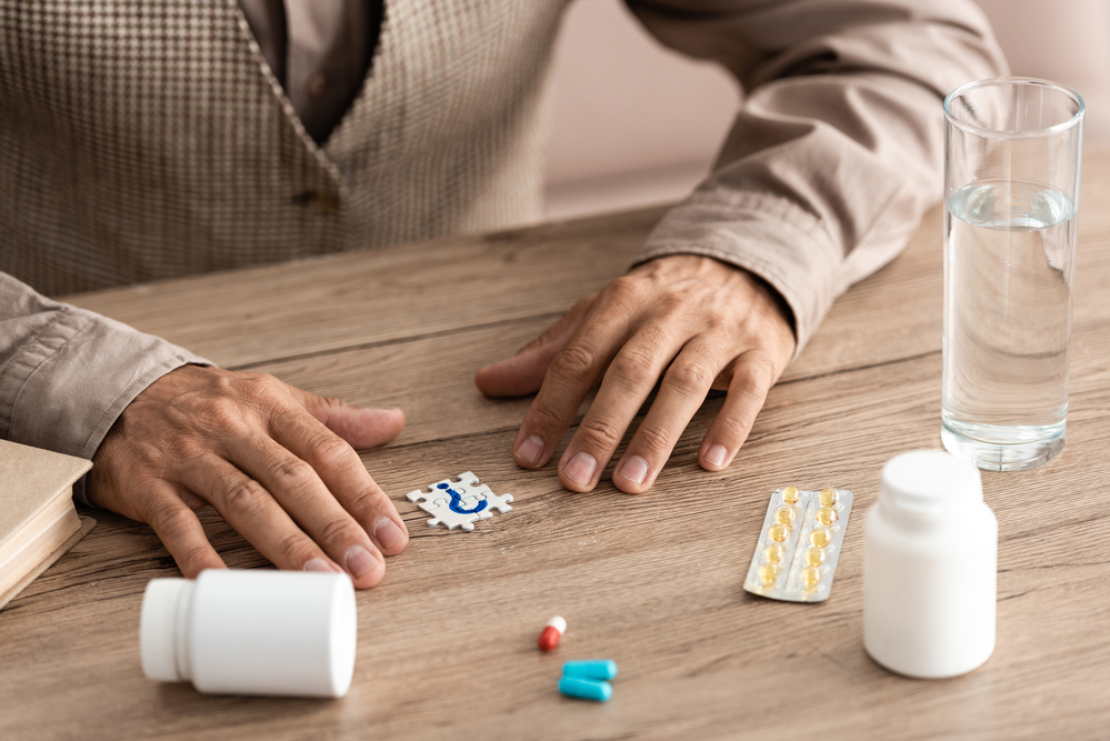 A paper with a question mark on it rests between some pills and a man's hands on a table