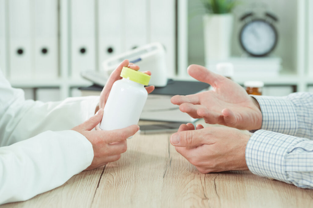 closeup photo of two people's hands; one holding a pill bottle and one making a questioning gesture