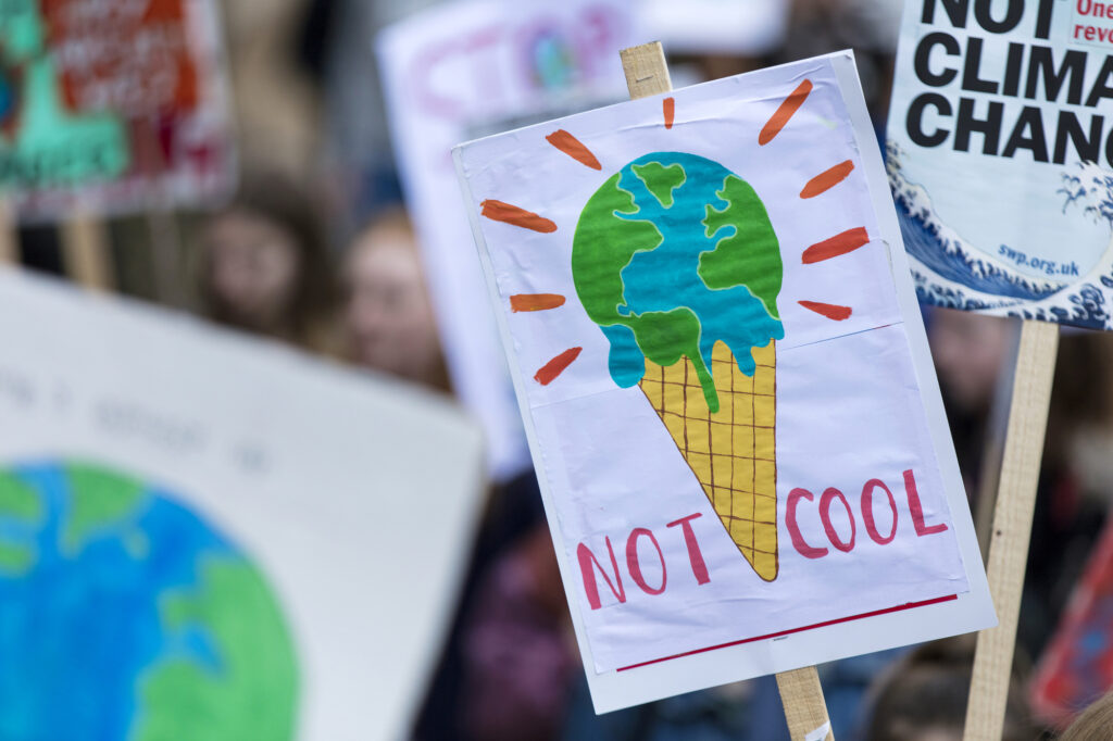 A sign at a climate change protest reads "NOT COOL" and depicts Earth as melting ice cream