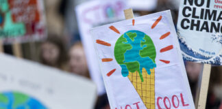 What Is Climate Distress—And What Can Therapists Do About It? A sign at a climate change protest reads "NOT COOL" and depicts Earth as melting ice cream