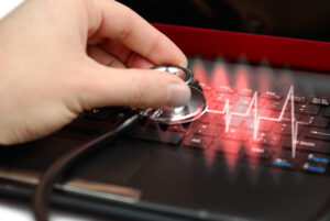 Close up of a stethoscope held to a computer, with a red diagnostic glowing out from it