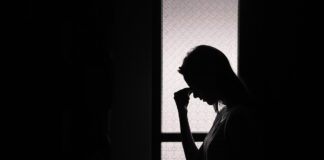 Mental Health Care Must Support Consent and Basic Human Rights Photo of a person sihouetted against a window holding their face with their hand, looking sad or in pain