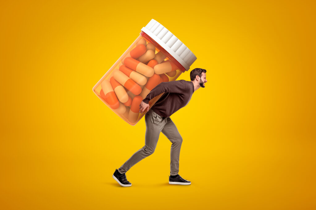 Side view of young man in casual clothes carrying big heavy-looking medicine jar on yellow background. 