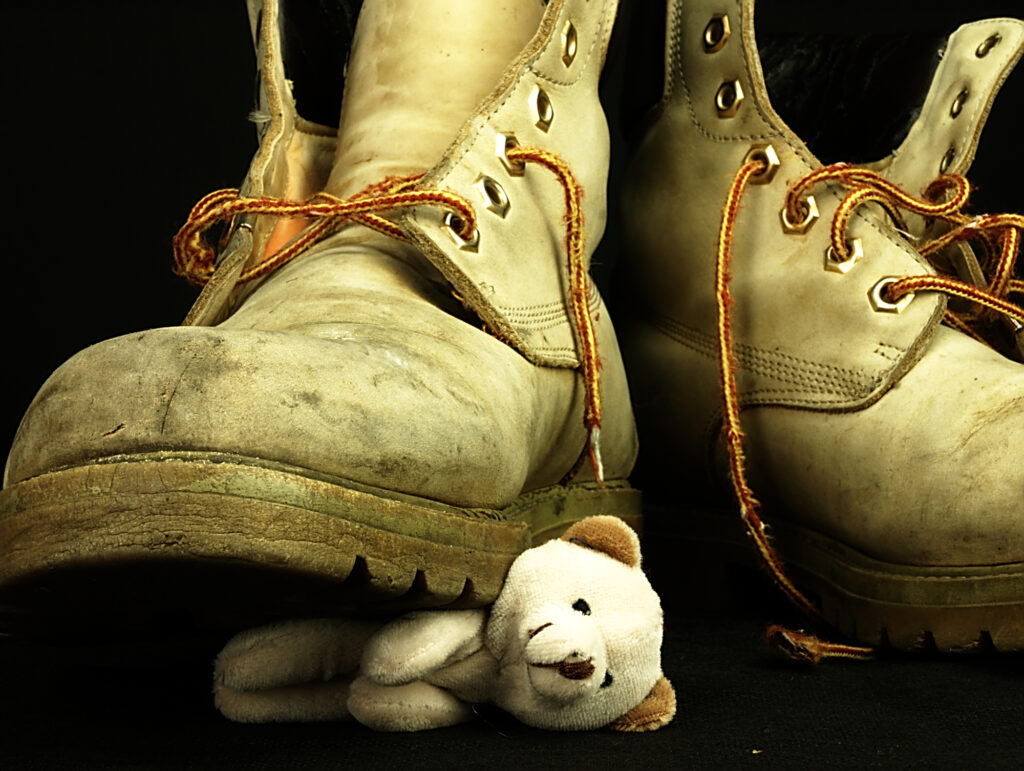 A photo of a teddy bear being stepped on by a work boot