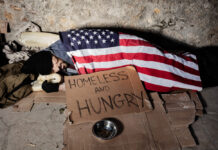Deaths of Despair on the Rise in the United States Homeless man begging for alms, sleeping on the sidewalk floor covered with American flag