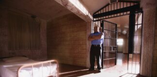 Inside a Forensic Psychiatry Unit: Earning the Right to Sleep on the Floor Photo of a prison cell with an uncomfortable-looking bed in the corner; a guard stands by the door