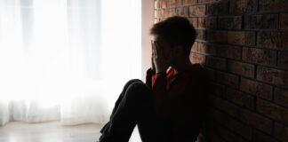 Why Is Child Sexual Abuse So Common in Institutions? Photo of a boy sitting against a brick wall with his hands covering his face