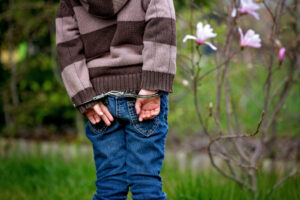 young boy in handcuffs facing a garden