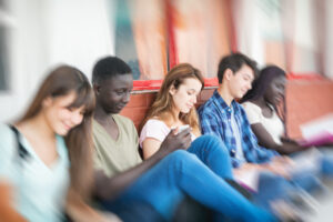 Teenagers in school hallway with notebooks and smartphones.