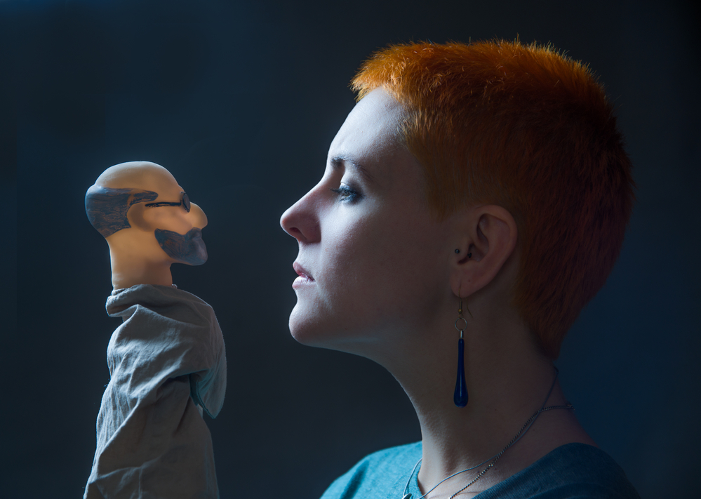 Against a dark background, profile of a young woman, the gaze which is directed at the doll depicting of Freud.