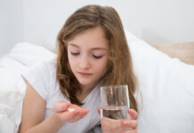 Meta-analysis Finds Antidepressants Ineffective for Children and Adolescents Girl On Bed Taking Pill With Glass Of Water In Bedroom