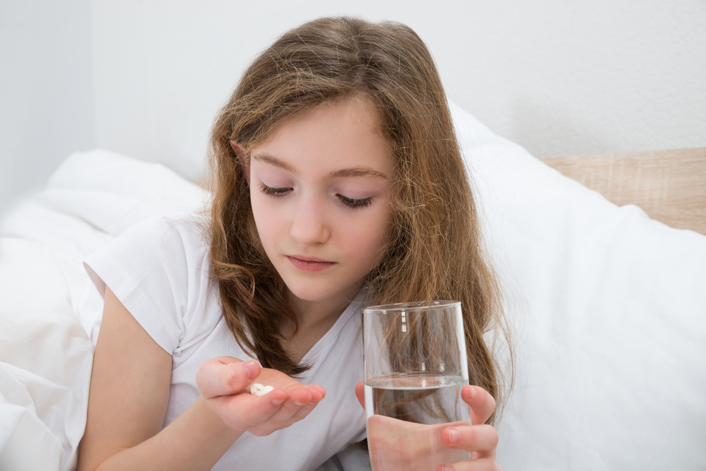 Girl On Bed Taking Pill With Glass Of Water In Bedroom