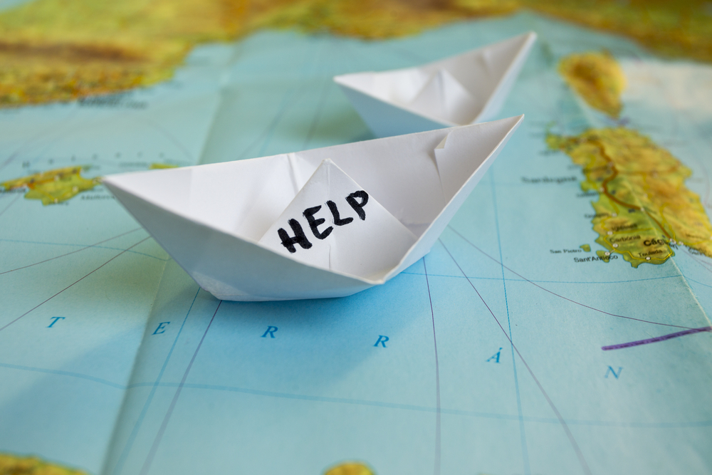 White paper boat onto world map with "Help" sign on it.