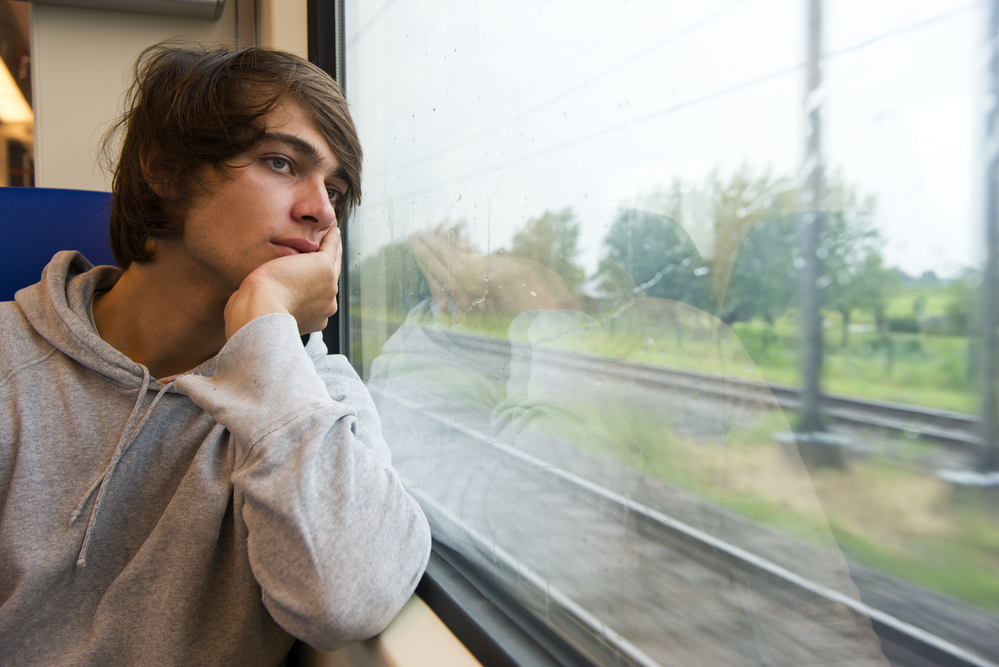 Bored young man, staring out the train window on a rainy, grey and dull day