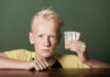 Risk of Depression Spikes When Kids Take Ritalin Scowling teenage boy holding up pills sealed in blister packs in his hand as he leans on a wooden table with an intense stare