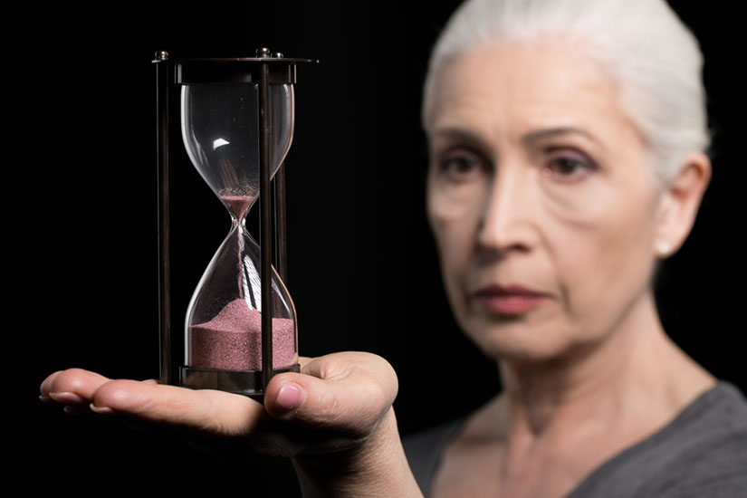 An older woman holds an hourglass