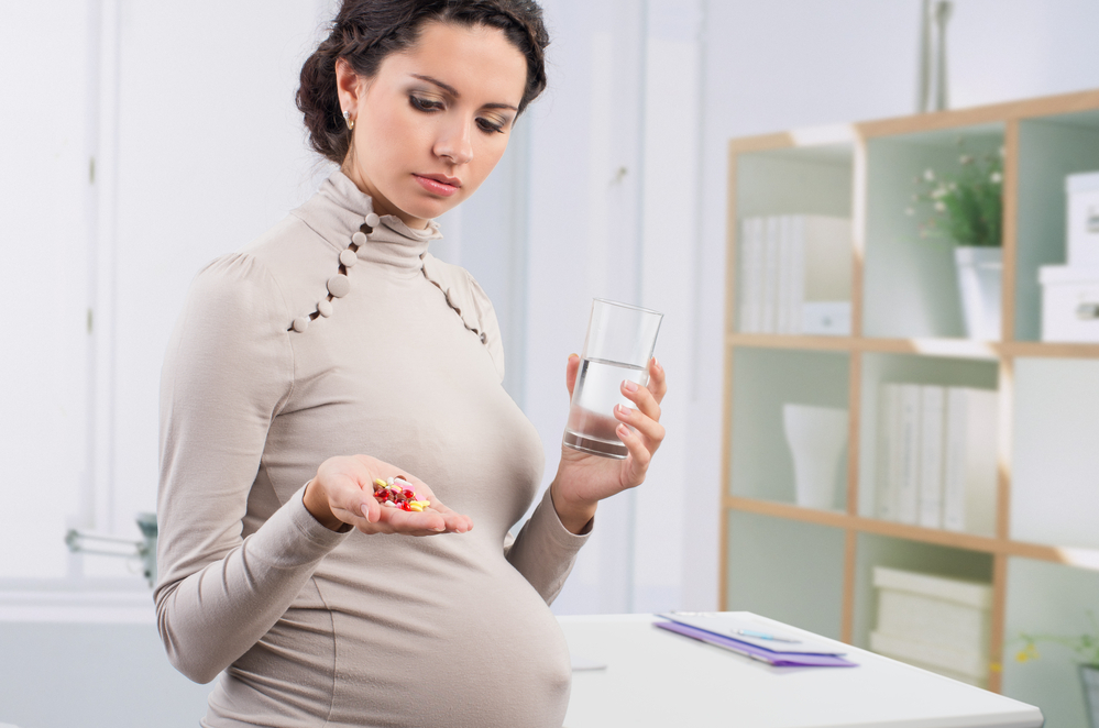 Pregnant woman holding pills and glass of water in hand