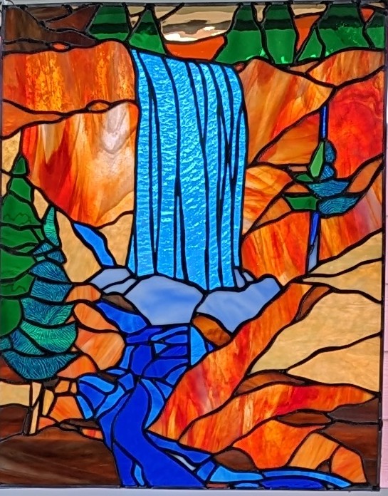 Stained glass picture of a waterfall with pine trees and bright orange mountains