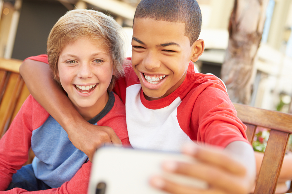 Two Boys Sitting On Bench In Mall Taking Selfie