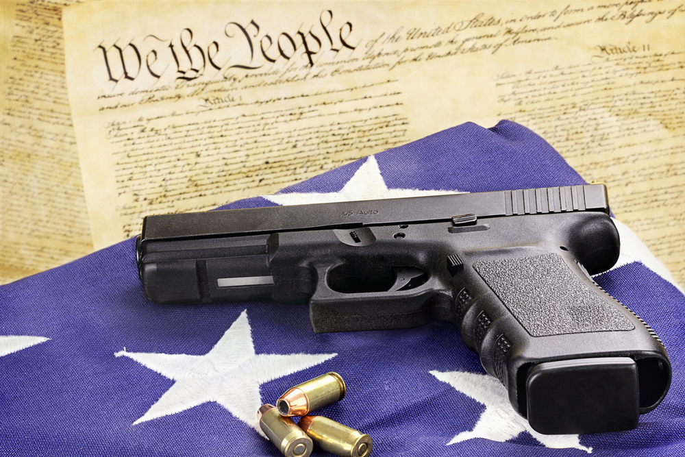 A 45 caliber handgun and ammunition resting on a folded flag against the United States constitution.