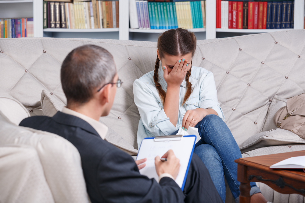 Teenage girl crying on sofa during therapy session