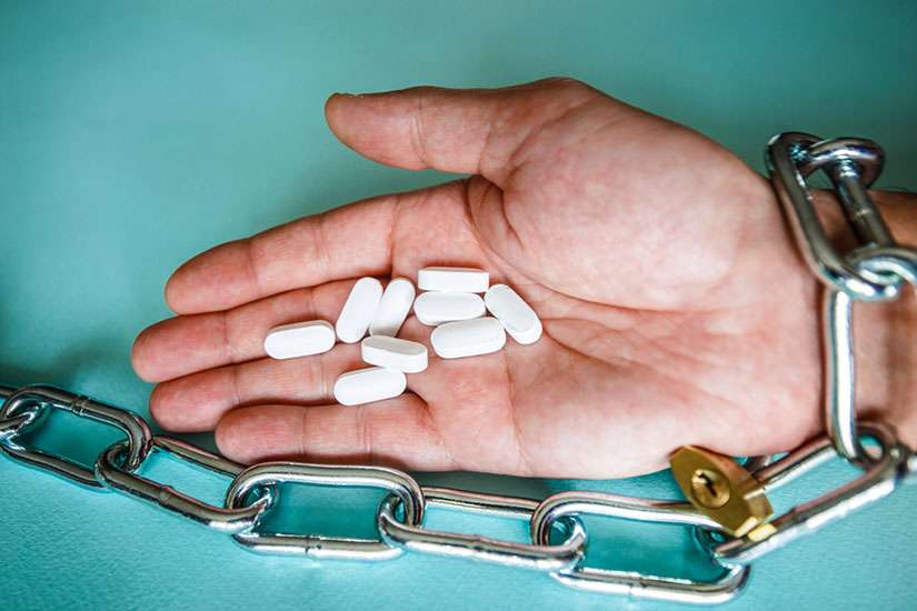 A hand chained in a chain holds pills