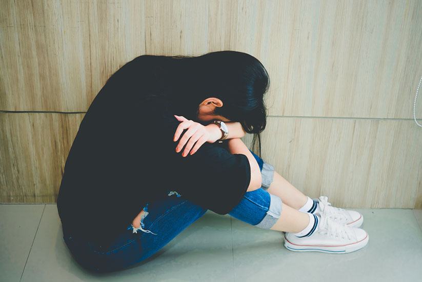 A photo of an Asian woman sitting on the floor, covering her face in sadness