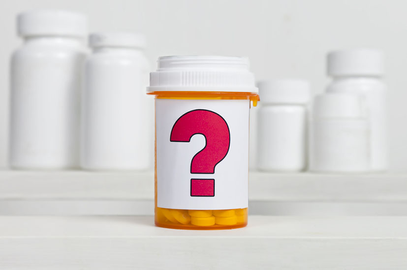 A pill bottle with a question mark on its label in front of other bottles.