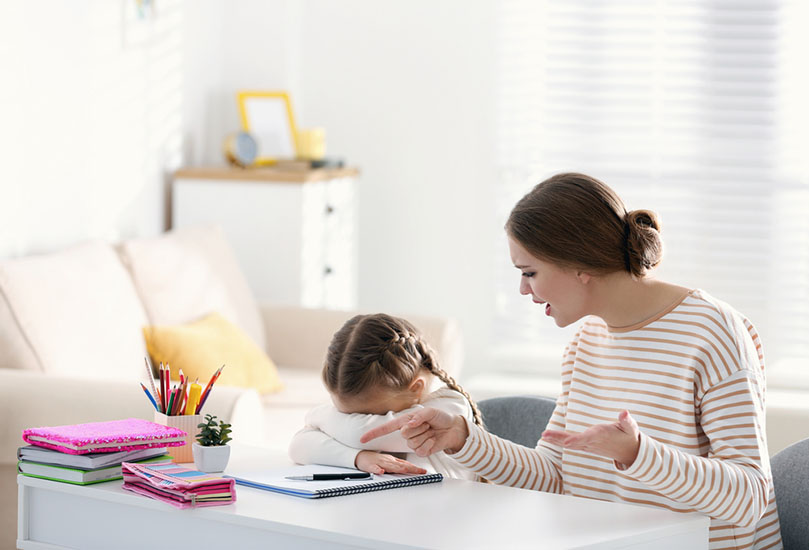 Stock photo of unhappy little girl; adult woman is trying to make her do worksheets