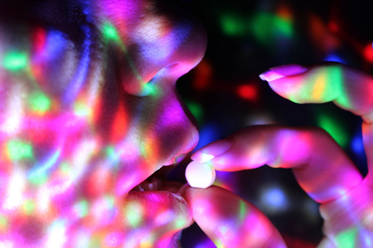 Close up of fingers putting a pill into a mouth. Colored lights all around