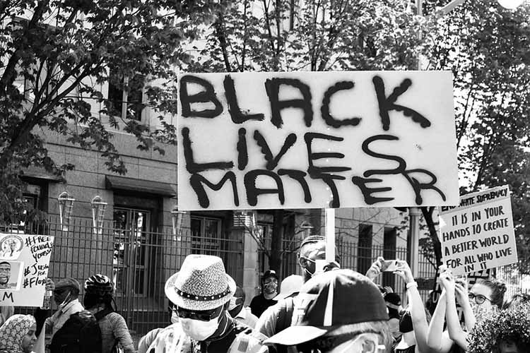 Black-and-white photo depicting protestor holding sign reading "BLACK LIVES MATTER"