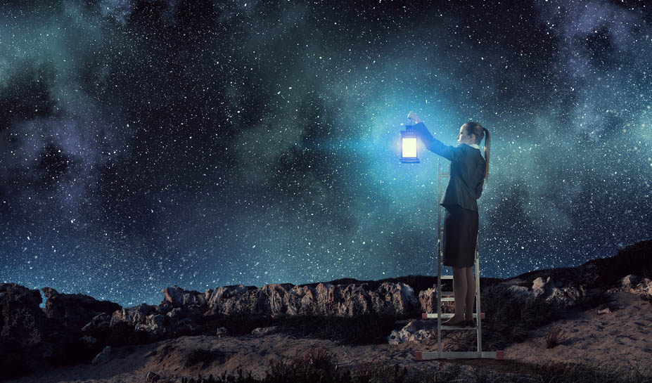 A woman in a suit with a skirt holds a lantern while standing on a desert landscape below a night sky full of stars