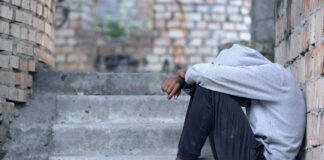 The “S” Word: How the Culture of Fear Has Failed Youth in Crises A black teen in a hooded sweatshirt sits on the stairs, hiding their face, looking depressed.
