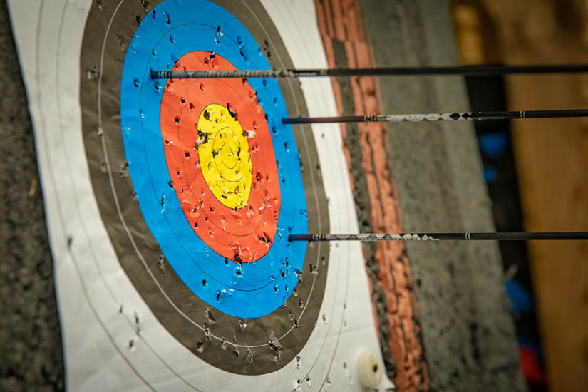 A photograph of an archery target with three arrows in it. None have hit the bullseye.